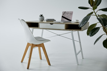 work table with laptop, books, flowerpot and white chair on grey