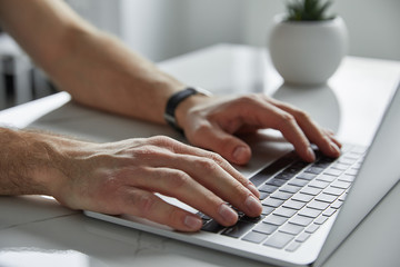 cropped view of man using laptop with black keypad on white marble table