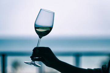 Silhouette image of a woman's hand holding a wine glass with blurred sea background