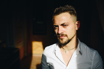 Close up portrait of young man wearing white shirt on street. Dramatic sun light. Fashion concept. Religion and emotion of theater