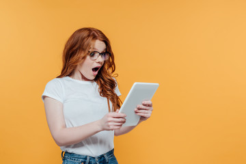 Fototapeta premium surprised redhead girl using digital tablet isolated on yellow with copy space