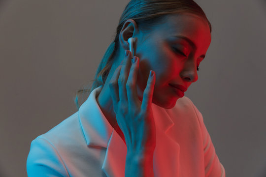 Photo closeup of fashion woman 20s wearing earpods looking at camera while standing under neon lights