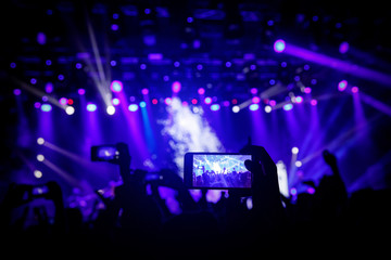 Smartphone in hand at a concert, blue light from stage