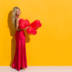 Beautiful Woman In Elegant Red Dress Is Posing With Heart Shaped Balloons