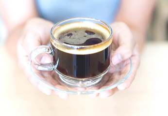 Closeup woman hand holding glass of hot americano coffee, selective focus, vintage tone