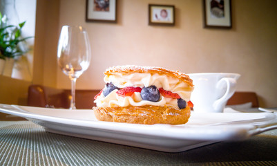 Cake with cream, strawberries and blueberries on a white plate on a table in a cafe 