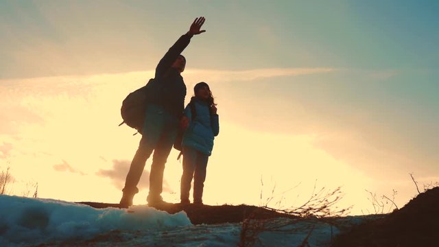 father and daughter teamwork happy family tourists silhouette concept navigation . team dad and daughter on top of a mountain at sunset raise shows the direction of the road with backpacks. winning