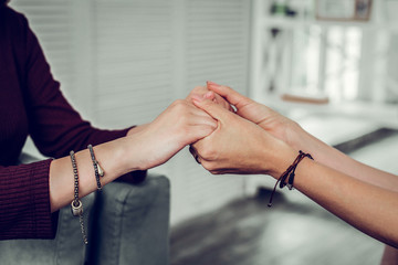 Obraz na płótnie Canvas Supportive psychologist wearing bracelets shaking hands of client
