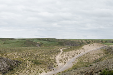 Automobile dirt and dusty roads among green hills and rocks in the mountainous region of Kazakhstan.