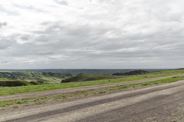 Fototapeta premium Automobile dirt and dusty roads among green hills and rocks in the mountainous region of Kazakhstan.
