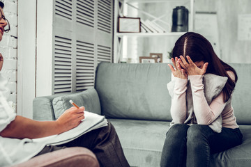 Dark-haired young woman hiding her face from psychologist