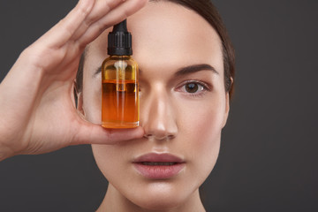 Fototapeta premium Charming young woman covering eye with vitamin serum