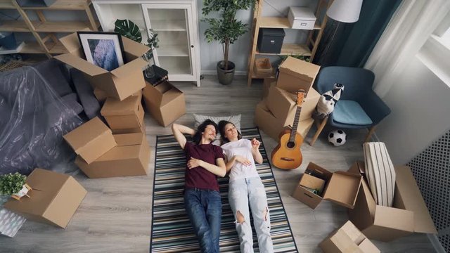Girl and guy are chatting and gesturing lying on floor after moving to new apartment together. Relocation, happy young family and modern lifestyle concept.