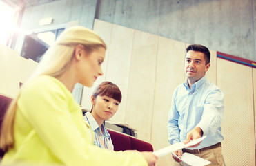 education, high school, university, learning and people concept - teacher giving exam tests to students at lecture