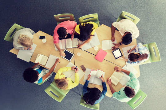 education, high school, people and technology concept - group of international students sitting at table with tablet pc computers, books and notebooks at university library from top
