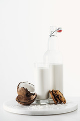 coconut vegan milk in glass and bottle near coconut and chocolate cookies isolated on white