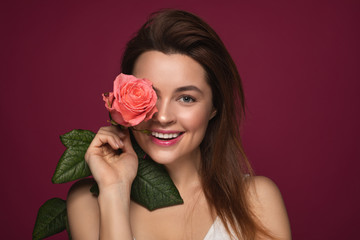 Long haired woman smiling while standing with pink rose