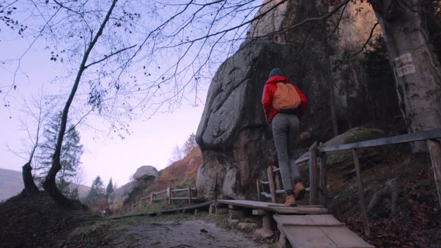 prety woman tourist walking on the wooden trail between rocks in the national park at sunrise with rocks background, back view. Excursion in Tustan, Ukraine. Tustan is a unique monument of history and