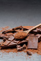 Dark or milk organic chocolate pieces and cocoa powder on dark concrete backgound