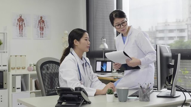 slow motion female doctor and nurse coworker discussing over a medical report in hospital. two asian girl medical staff talking in working office on computer desktop pointing finger hand to screen.