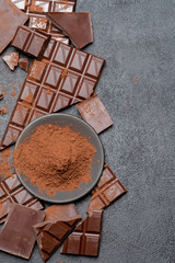 Frame or border made of Dark or milk organic chocolate pieces and cocoa powder on dark concrete backgound