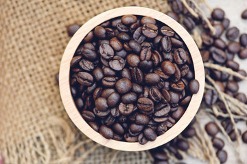Fototapeta premium Roasted coffee beans in sack background / Closeup macro of coffee beans on wooden bowl - top view