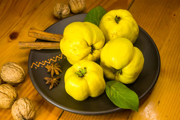 large yellow quince fruits on a ceramic plate, with anise, cinnamon, and walnuts