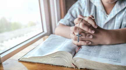 Close up hands of christian boy holding silver cross and praying on holy bible. religion concept.