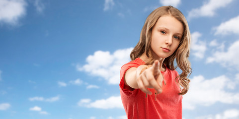 accusing gesture and people concept - teenage girl with long hair in red t-shirt pointing finger to you over blue sky and clouds background