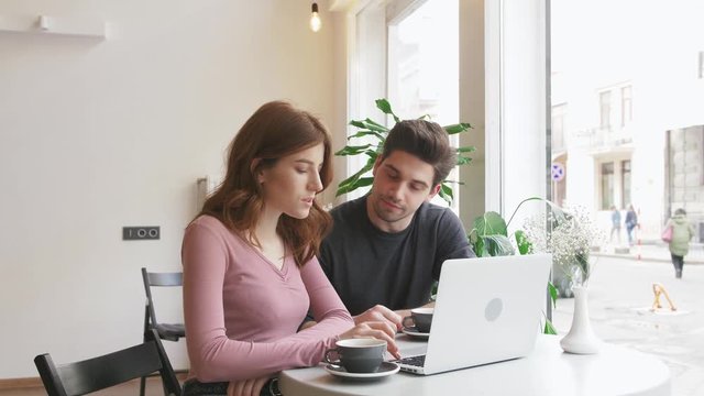 Two young people working with a laptop in a cafe and drinking coffee, slow motion
