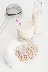 chickpea in white cheesecloth near bottle and glass with vegan chickpea milk and sieve on grey background