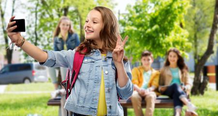 education, school and people concept - happy smiling teenage student girl with bag taking selfie by smartphone and showing peace over group of friends background