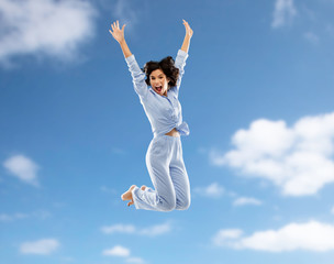 fun, people and bedtime concept - happy young woman full of energy in blue pajama jumping over blue...