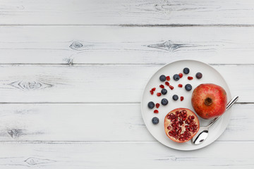 Fototapeta na wymiar blueberries and pomegranate with a silver spoon on a plate on distressed white wood