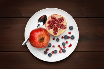 blueberries and pomegranate with a silver spoon on white plate