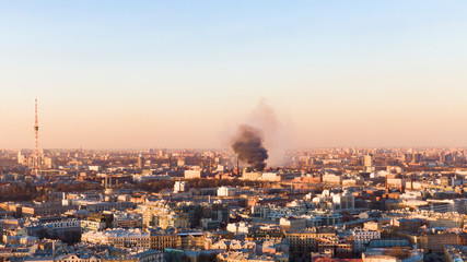 Black smoke rises above the horizon in the city, the building burns. Aerial view at sunset