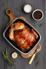 roast chicken in a rasting tin with ingredients and carving fork on dark grey wood