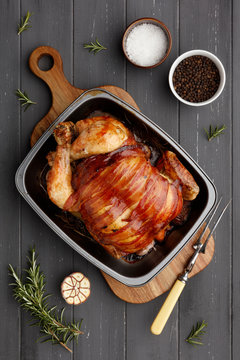roast chicken in a rasting tin with ingredients and carving fork on dark grey wood