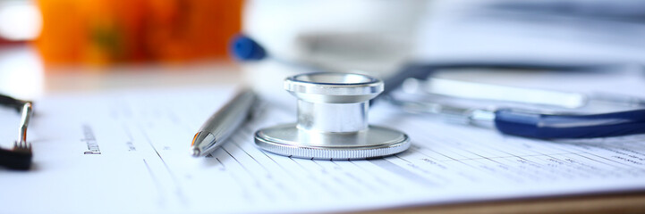 Stethoscope head and silver pen lying on medical application form