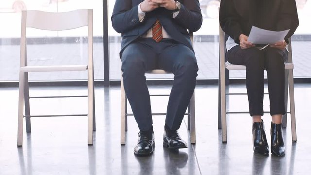 cropped view of women holding resume, man using smartphone while sitting on chair and waiting job interview then leaving 