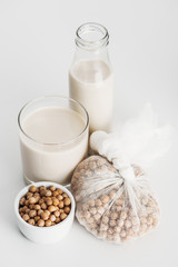 chickpea in bowl and cheesecloth near vegan chickpea milk in glass and bottle on grey background