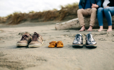Family shoes in the sand with pregnant woman in the background with her partner