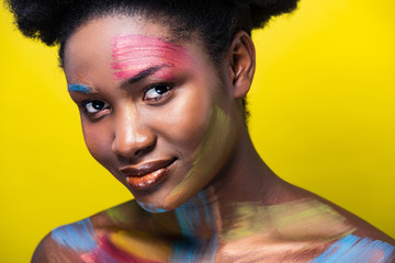 Smiling african american woman with bright makeup looking at camera isolated on yellow