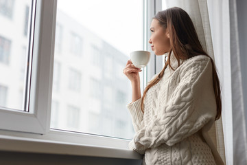 Relaxing dreaming woman with drink at window