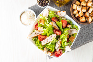 Fresh salad made of tomato, ruccola, chicken breast, eggs, arugula, crackers and spices. Caesar salad in a white, transparent bowl on wooden background