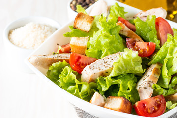 Fresh salad made of tomato, ruccola, chicken breast, eggs, arugula, crackers and spices. Caesar salad in a white, transparent bowl on wooden background
