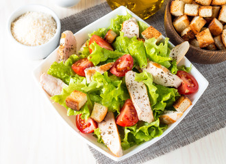 Fresh salad made of tomato, ruccola, chicken breast, eggs, arugula, crackers and spices. Caesar salad in a white, transparent bowl on wooden background