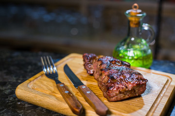 Juicy medium Beef Rib Eye steak on wooden board with fork and knife herbs spices and salt.