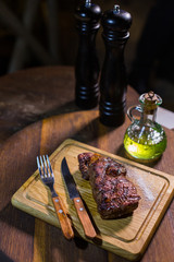 Juicy medium Beef Rib Eye steak on wooden board with fork and knife herbs spices and salt.
