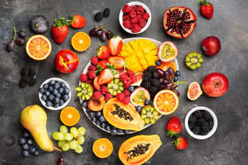 Delicious fruit platter mango pomegranate raspberries papaya oranges passion fruits berries on oval serving plate on dark concrete background, selective focus, top view